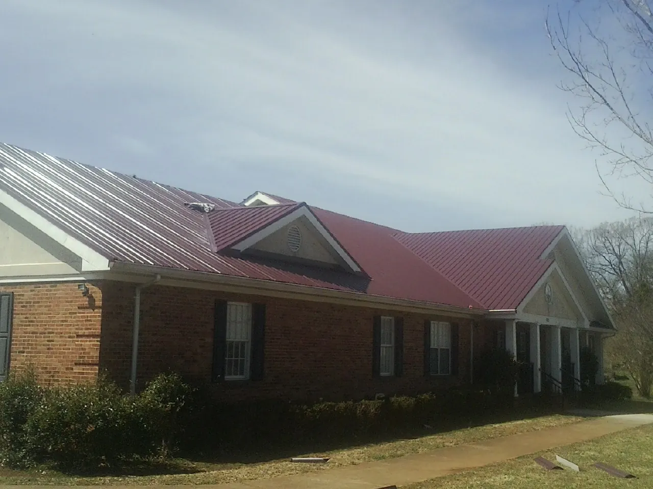 Red metal roof with gabled entries on a long brick building, from a Hail Damage Roof Repair job in Clarksburg